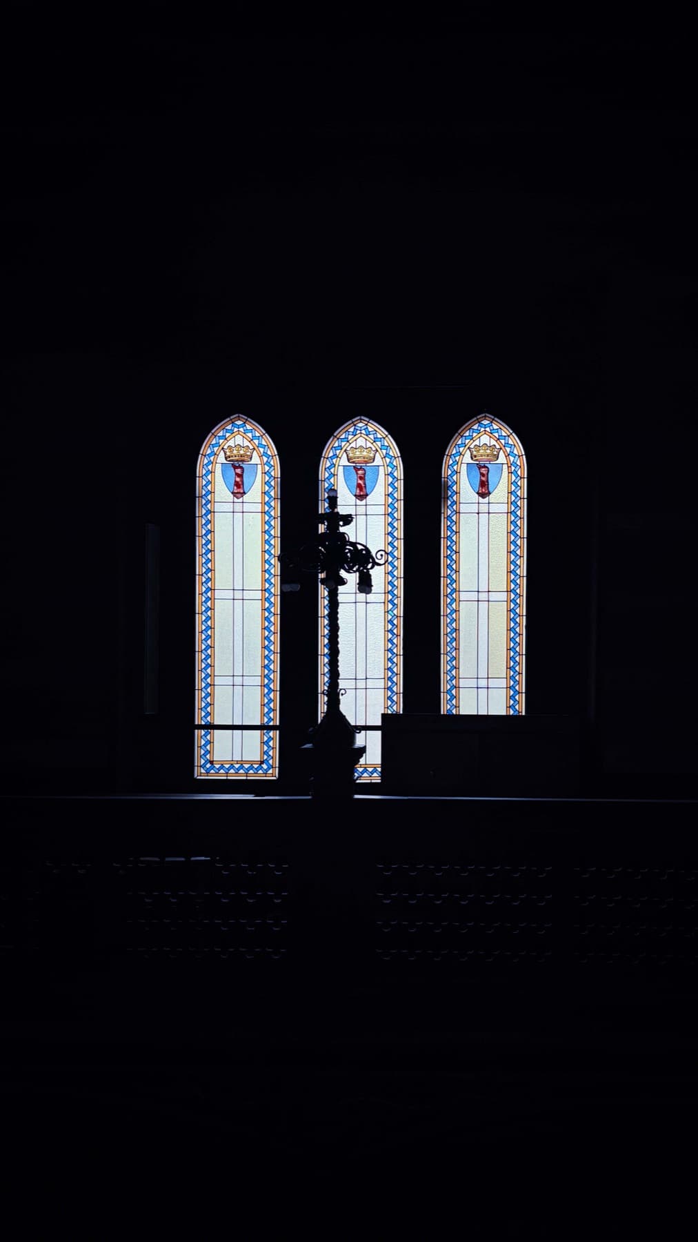 Three stained-glass arched windows bearing heraldic crests.